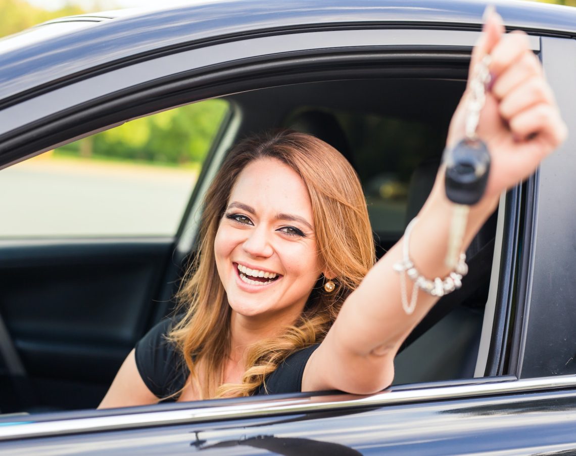 Young happy woman in the car with keys in hand - concept of buying car